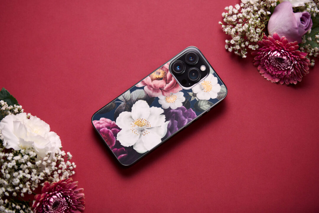 Product photo of a phone skin from Rabbiter with flowers on it. Surrounded with flowers on a red background for a beautiful and minimalistic look.