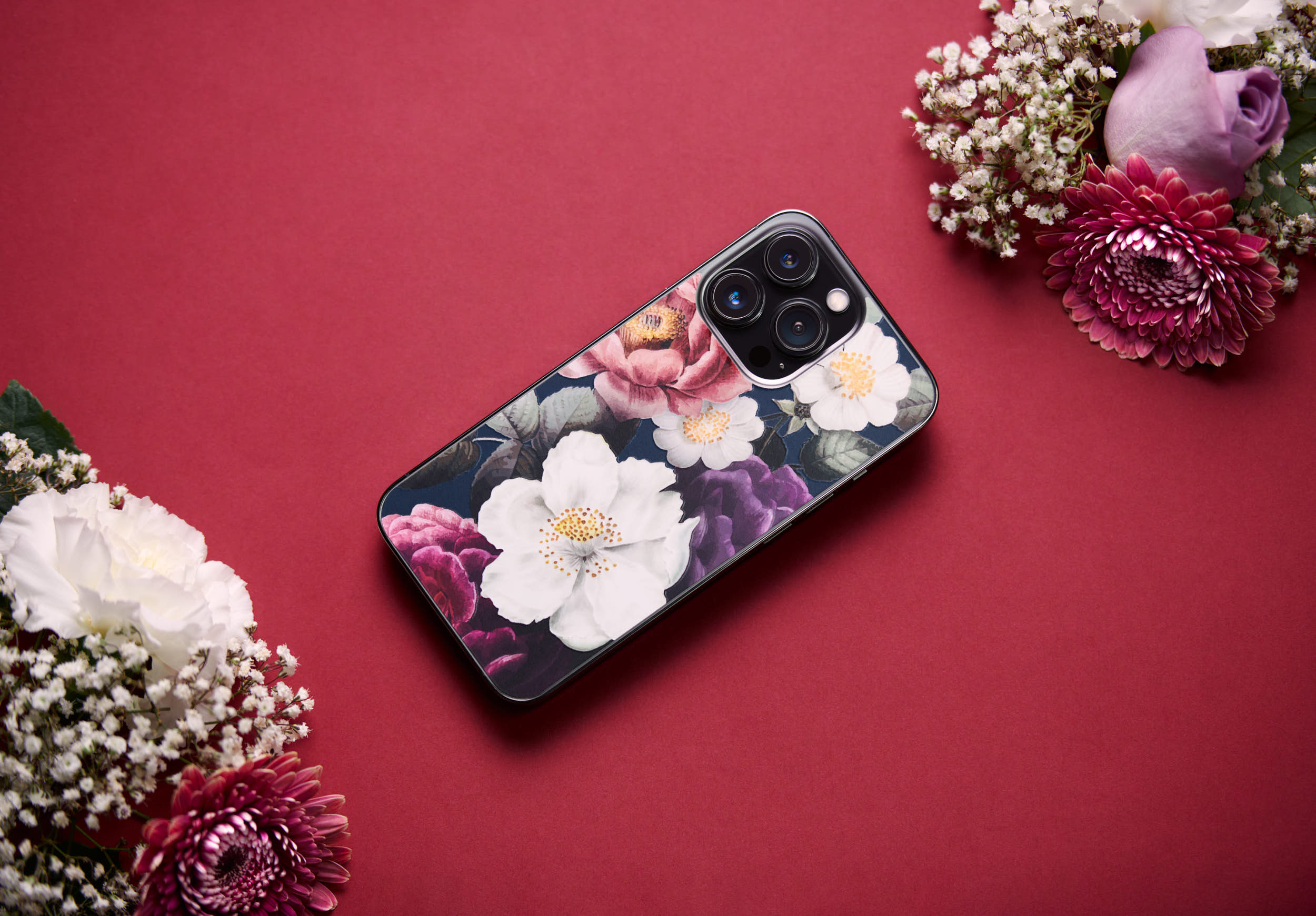 Product photo of a phone skin from Rabbiter with flowers on it. Surrounded with flowers on a red background for a beautiful and minimalistic look.