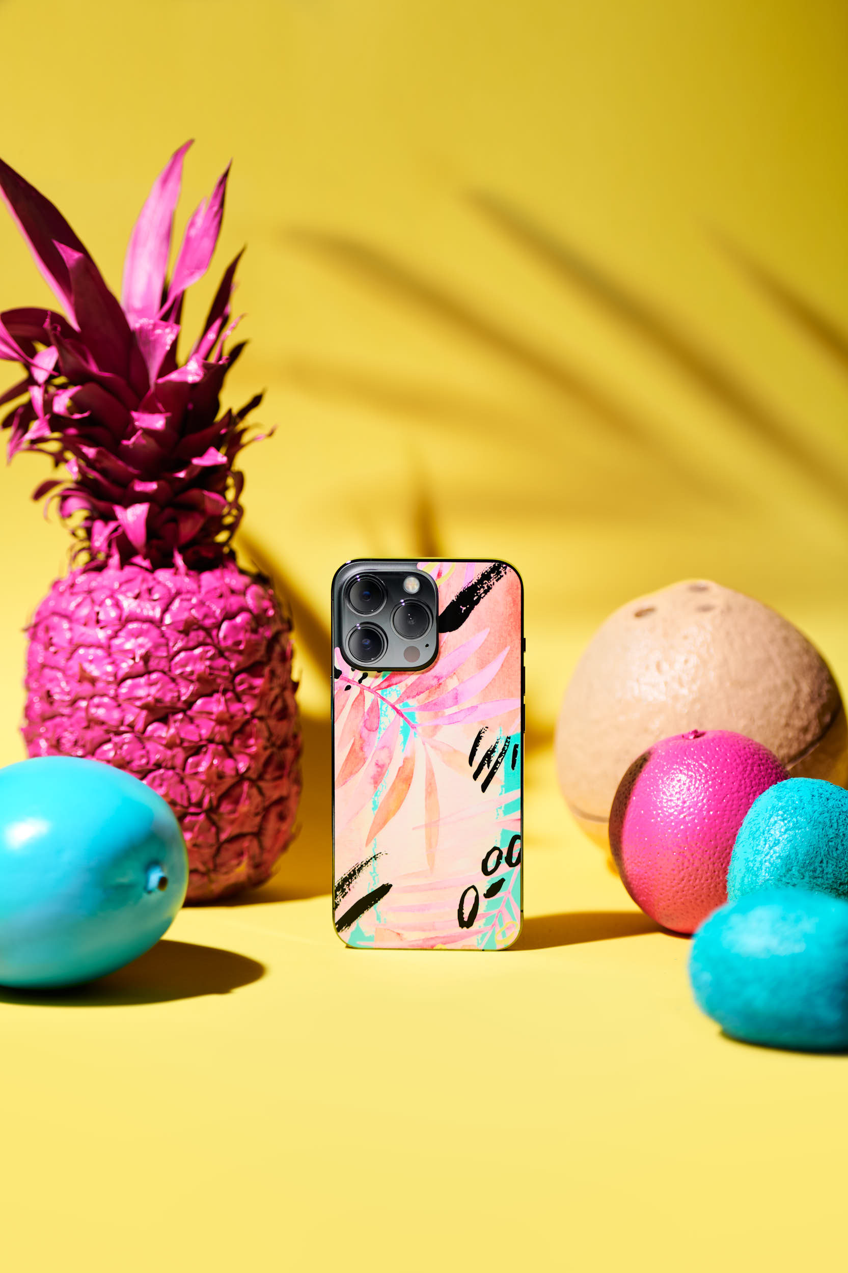 Product photo of a tropical phone skin from Rabbiter. Placed between tropical food colored in the Rabbiter skin colors for a fresh, modern feeling supported with a tropical sunlight and shadows.